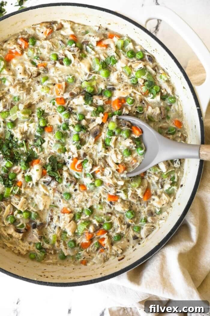 Close-up overhead shot of a creamy crustless chicken pot pie with chicken, peas, carrots, and mushrooms in a rustic skillet, garnished with fresh herbs.