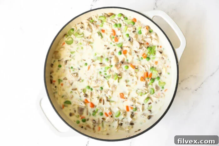 Crustless chicken pot pie cooking in a skillet, with creamy coconut milk being stirred into the mixture.