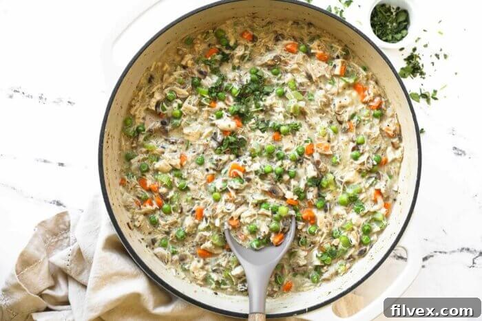 A fully cooked crustless chicken pot pie in a large skillet, garnished with fresh parsley, with a spoon sticking out, ready to serve.