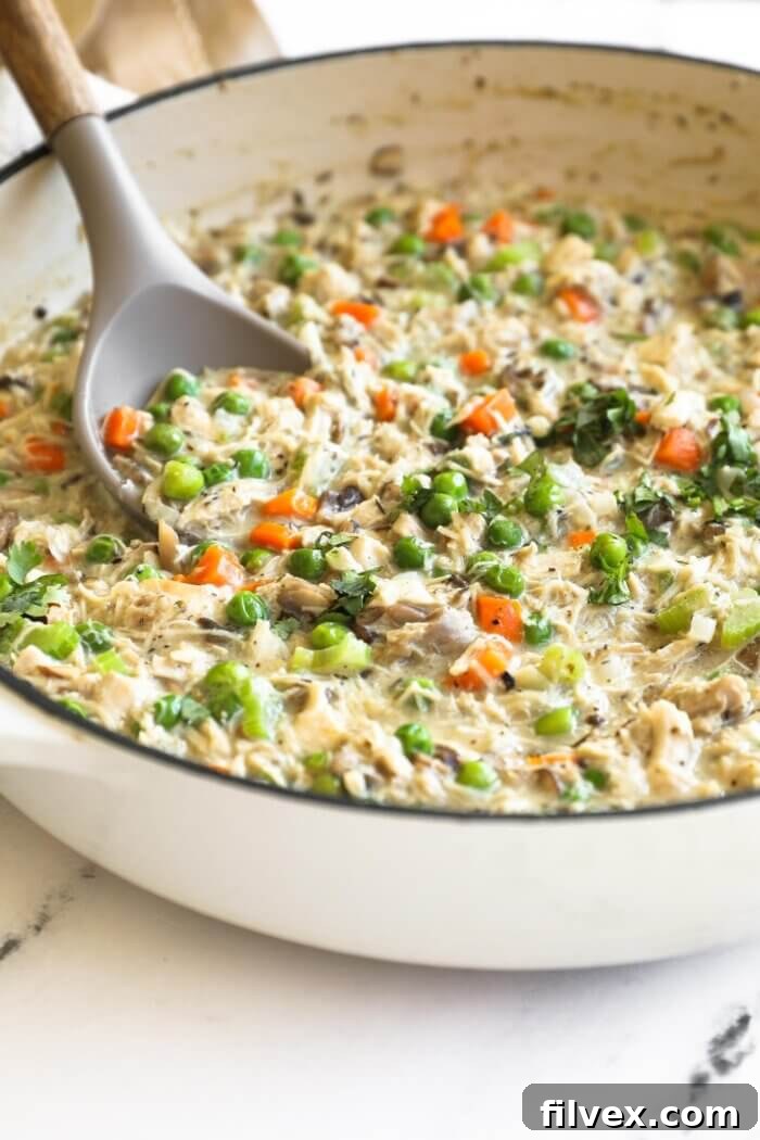 A large skillet filled with creamy crustless chicken pot pie mixture, showcasing visible pieces of chicken, carrots, peas, and mushrooms.