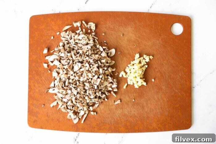 Chopped mushrooms and minced garlic cloves neatly arranged on a wooden cutting board, ready for cooking.
