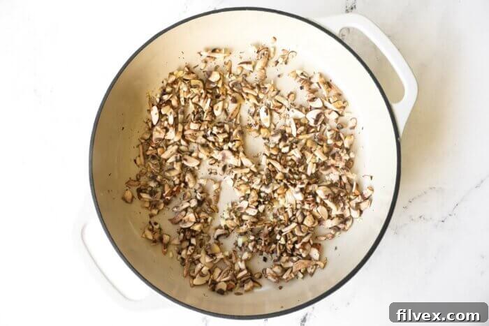 Close-up of chopped garlic and sliced mushrooms sizzling in a pan with melted ghee.