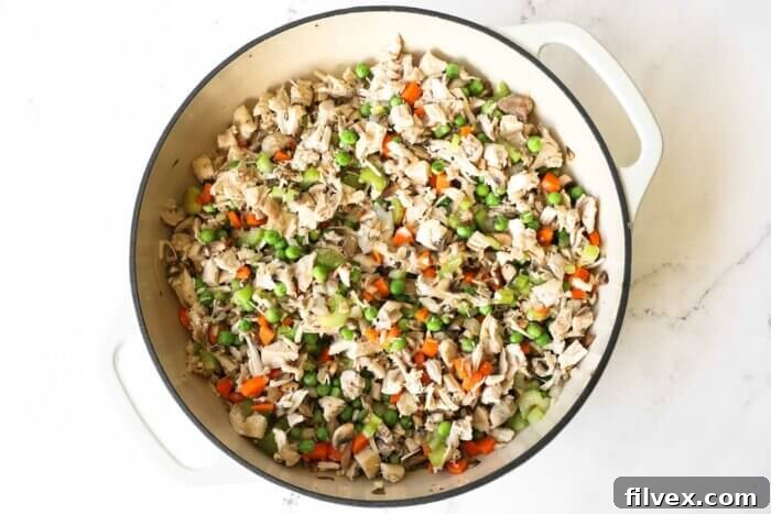 A mix of mirepoix vegetables (carrots, celery, onions) and cooked chicken simmering in a skillet.