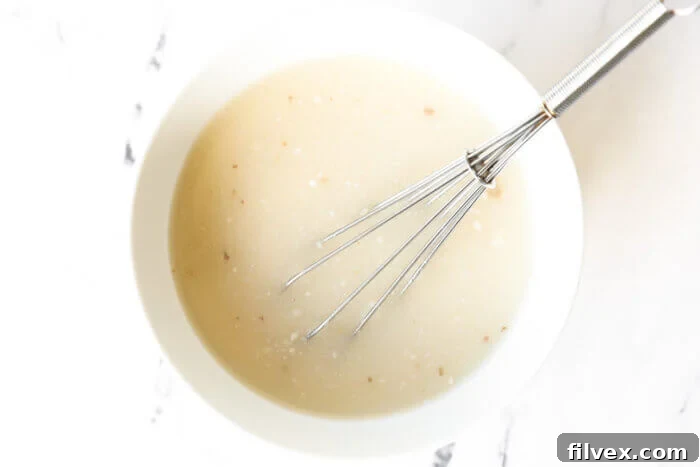 Chicken broth and tapioca starch being whisked together in a bowl, creating a smooth mixture.