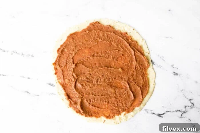 Burrito tortilla with refried beans spread out all over