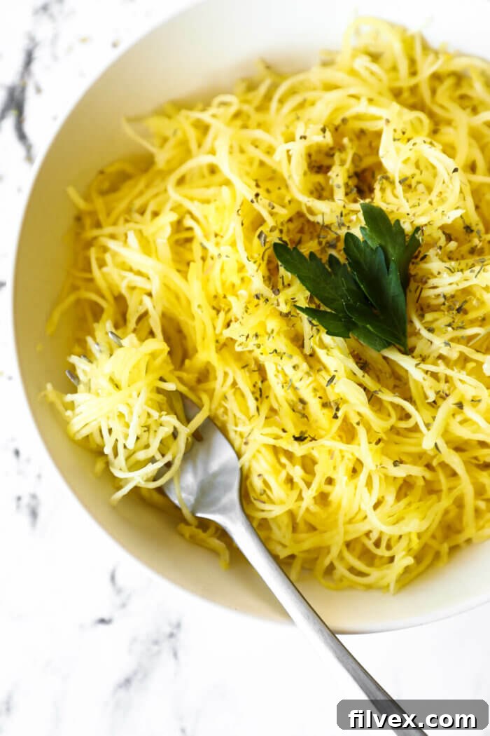 Overhead image of a bowl full of spaghetti squash noodles with herbs sprinkled on top. A fork is in the bowl with noodles wrapped around it.
