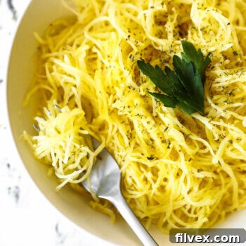 Overhead image of a bowl full of spaghetti squash noodles with herbs sprinkled on top. A fork is in the bowl with noodles wrapped around it.