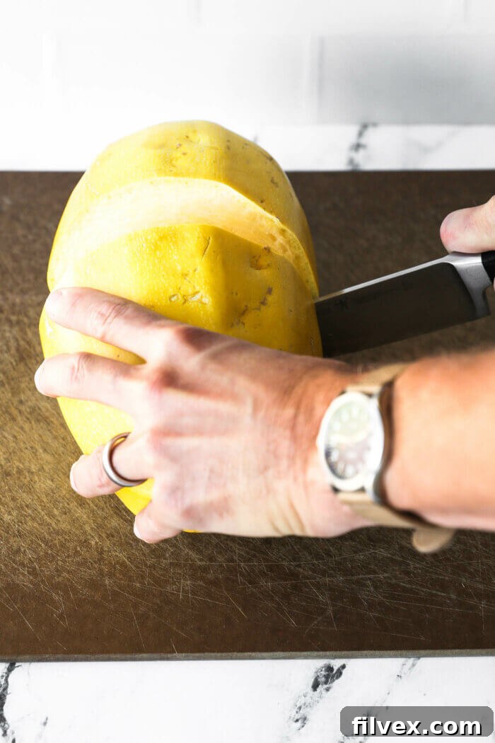 Image of someone cutting a spaghetti squash crosswise with a large chef's knife.