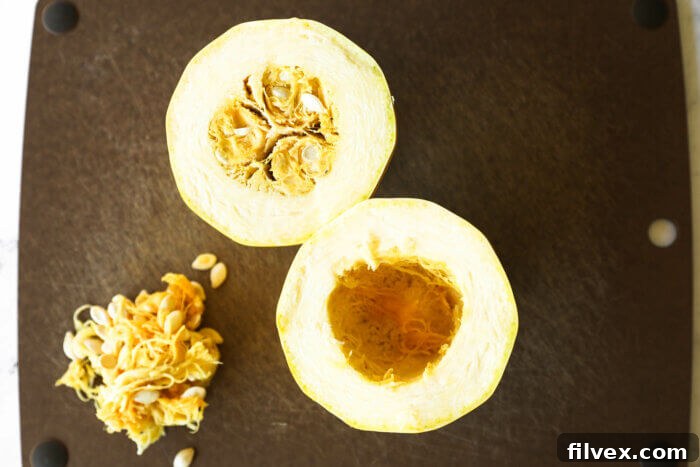 Image of spaghetti squash cut in half crosswise with the seeds scooped out of one side and in a pile on the cutting board.