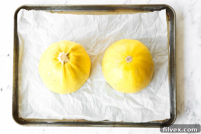 Spaghetti squash cut in half crosswise and placed open face down on a lined baking sheet to roast in the oven.
