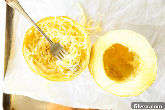 Roasted spaghetti squash on a baking sheet with the noodles scooped out in one half.