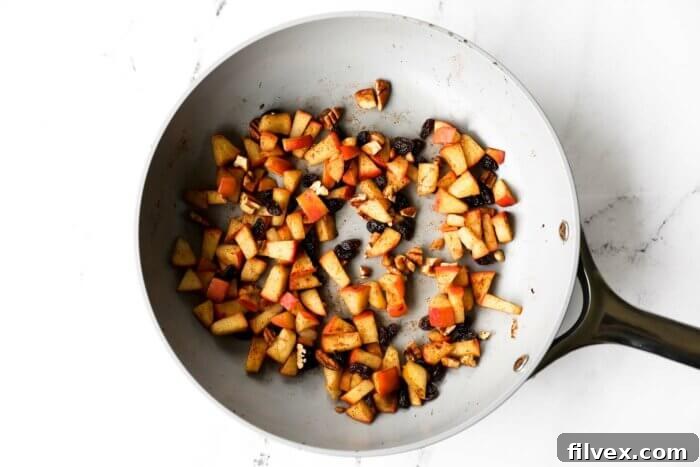 Apples, cinnamon, raisins and chopped pecans heated up in a skillet to serve as a pancake topping.