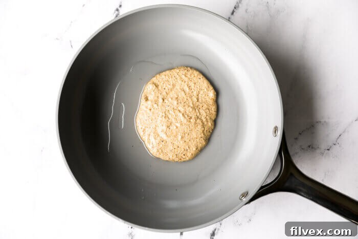 Oat flour pancake batter added to a hot skillet.