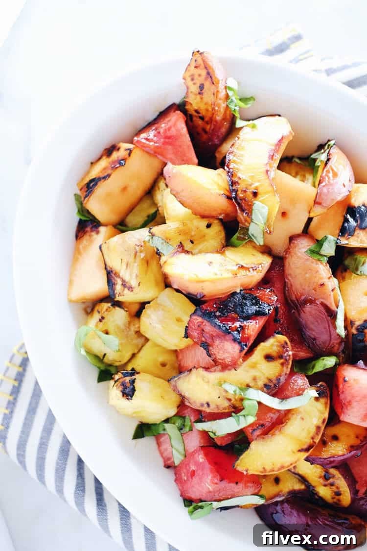 Bowl of grilled fruit salad with balsamic drizzle and fresh basil leaves.