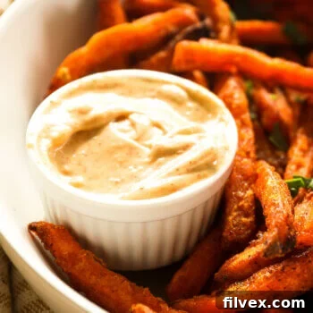 Close up angle image of sweet potato fries dipping sauce in a ramekin with a bowl of fries