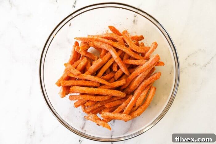Frozen sweet potato fries in a mixing bowl, tossed with oil and seasoning