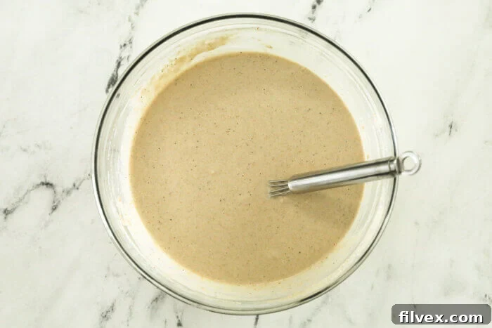 Overhead image of a mixing bowl with oat flour waffle batter and a whisk.