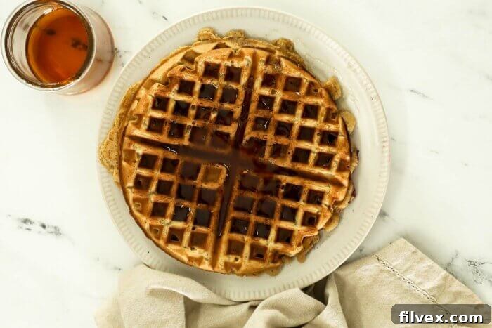 Image of cooked oat flour waffles on a plate with maple syrup on top.