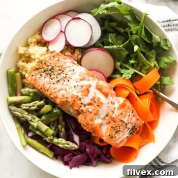 Close up overhead image of salmon buddha bowls over radish, arugula, millet, carrot, cabbage and asparagus
