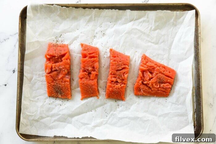 Raw salmon pieces on a sheet pan with salt and pepper
