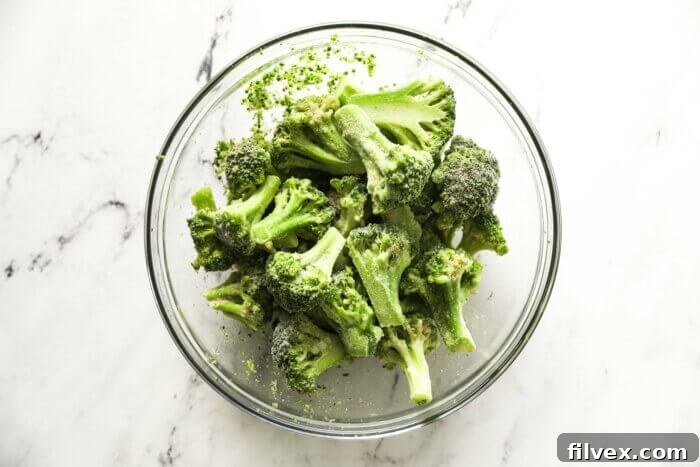 Frozen broccoli florets in a bowl, perfectly tossed with avocado oil and a savory seasoning blend, ready for the air fryer.