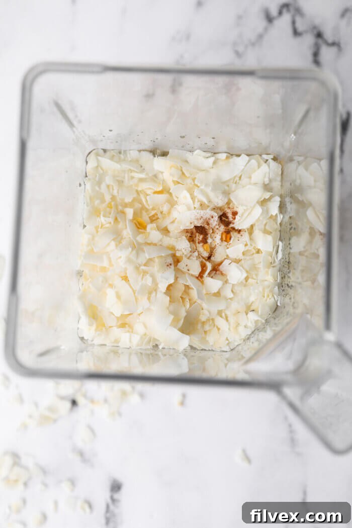 Overhead image of a blender with water, coconut flakes, maple syrup, vanilla and cinnamon before blending.