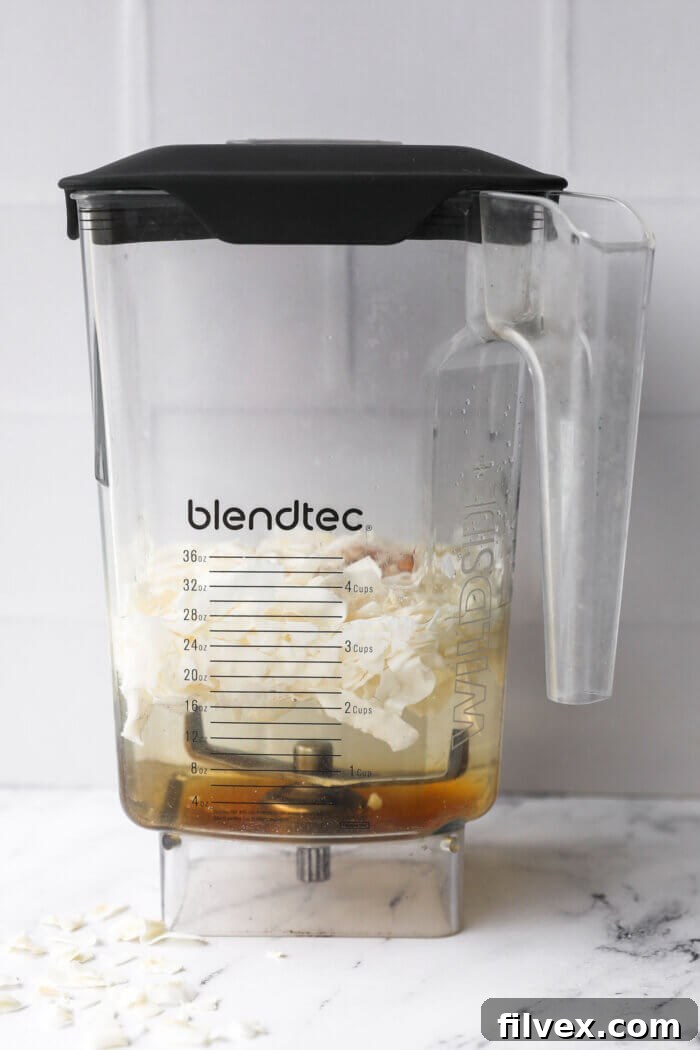 Straight on image of a blender with water, coconut flakes, maple syrup, vanilla and cinnamon before blending.