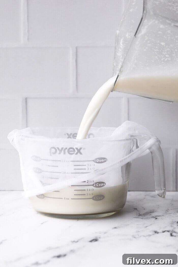 Pouring coconut milk in a jar with a nut milk bag for straining.
