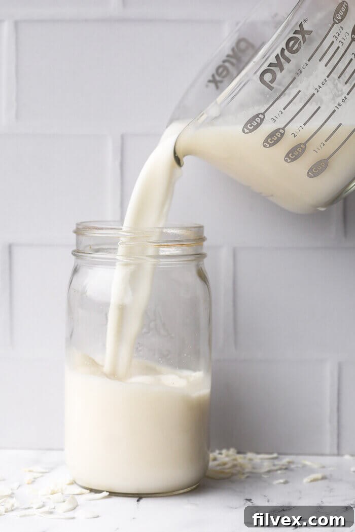 Pouring strained coconut milk into a mason jar for storing in the fridge.