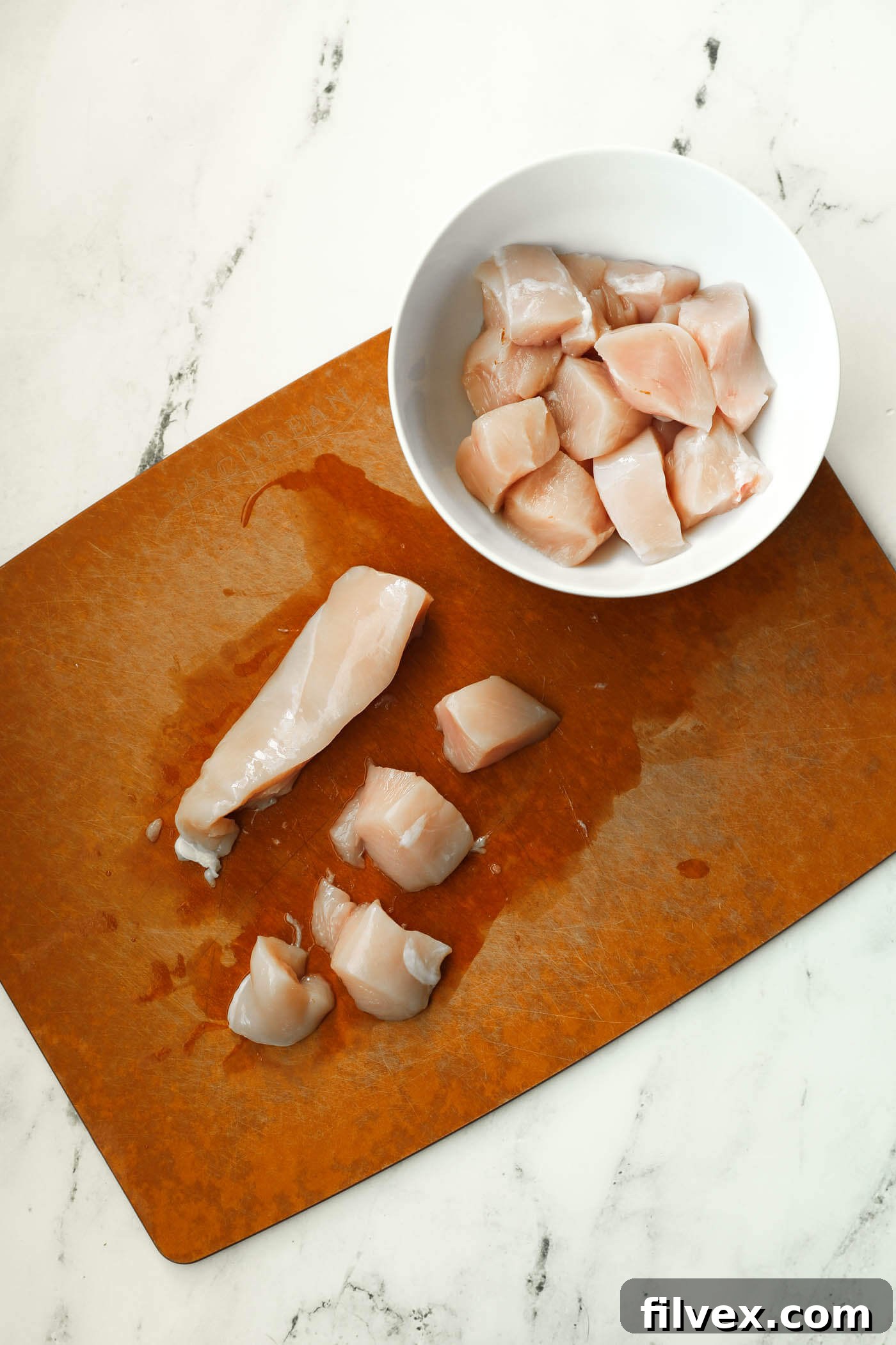 Chicken breasts being cut into uniform bite-sized pieces for keto nuggets.