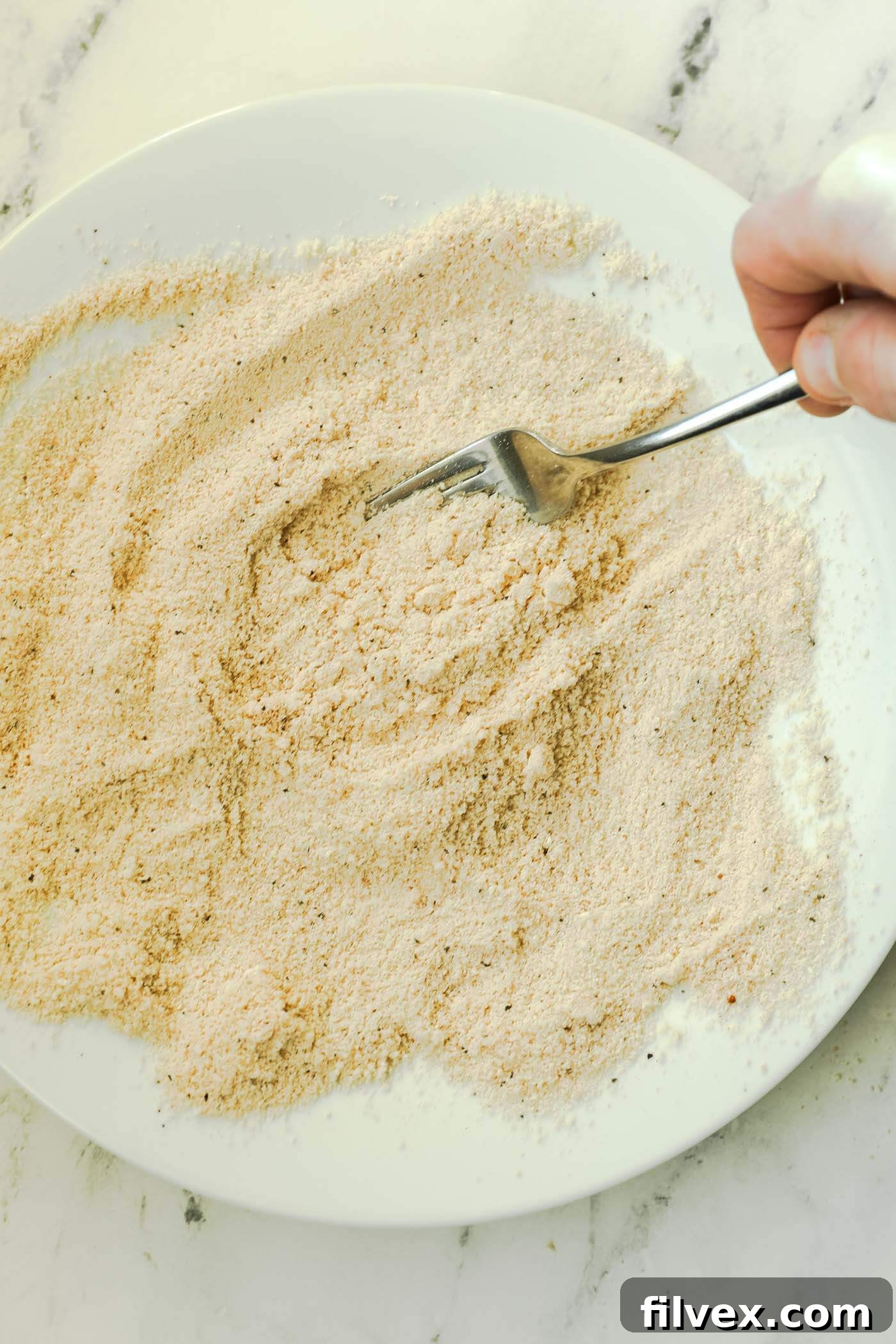 A fork mixing the flour and seasoning blend thoroughly on a plate.