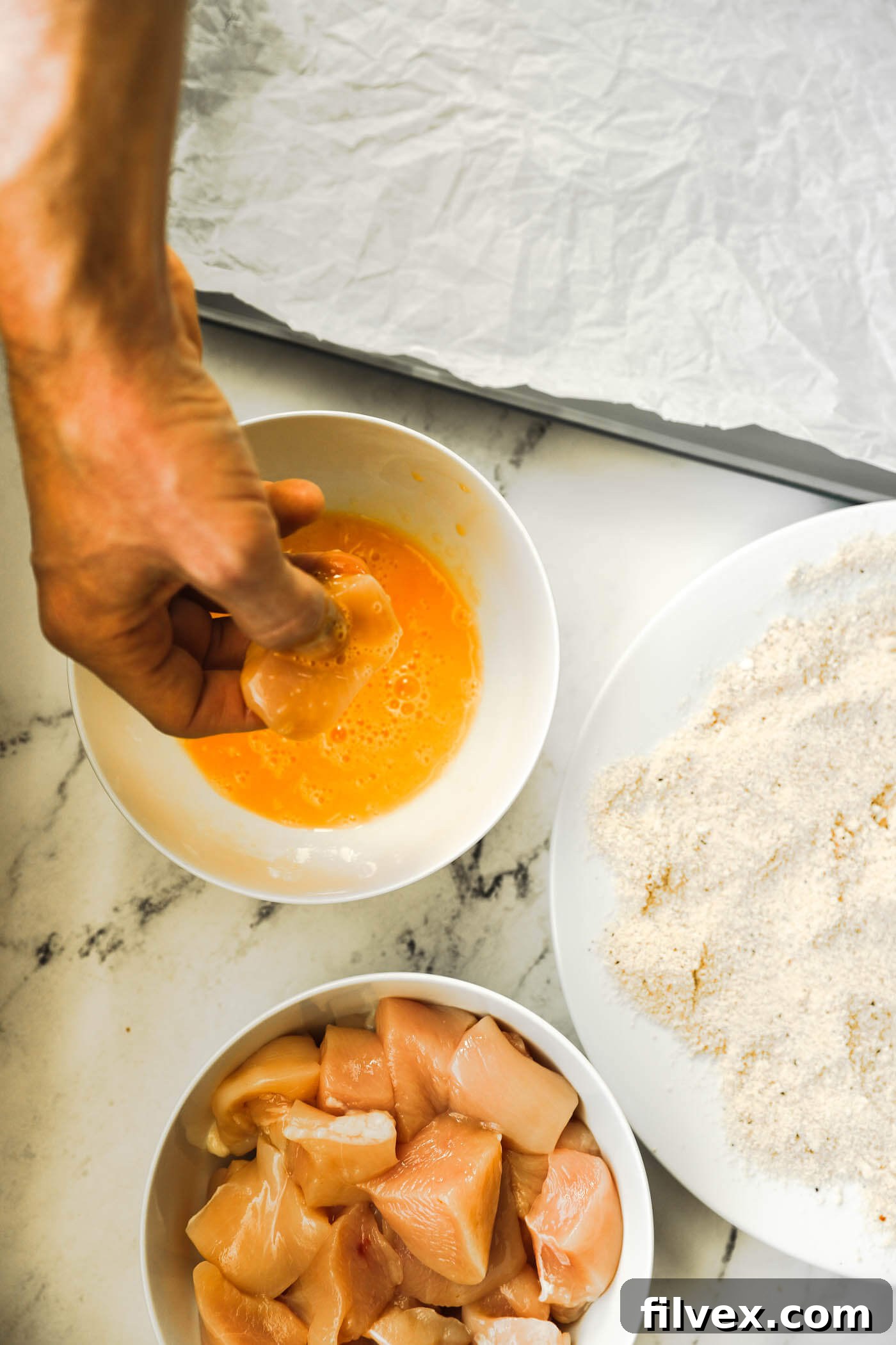 A chicken piece being dipped and coated in whisked egg.