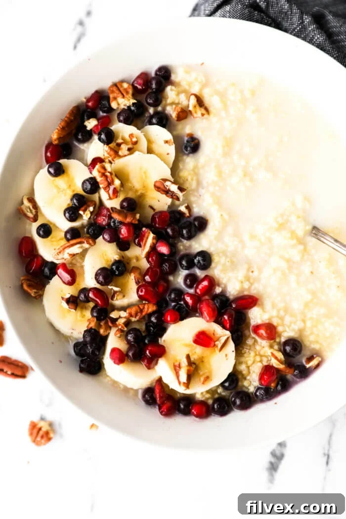 A bowl of creamy millet porridge generously topped with fresh berries, banana slices, pomegranate seeds, and chopped pecans, showcasing a vibrant and healthy breakfast.