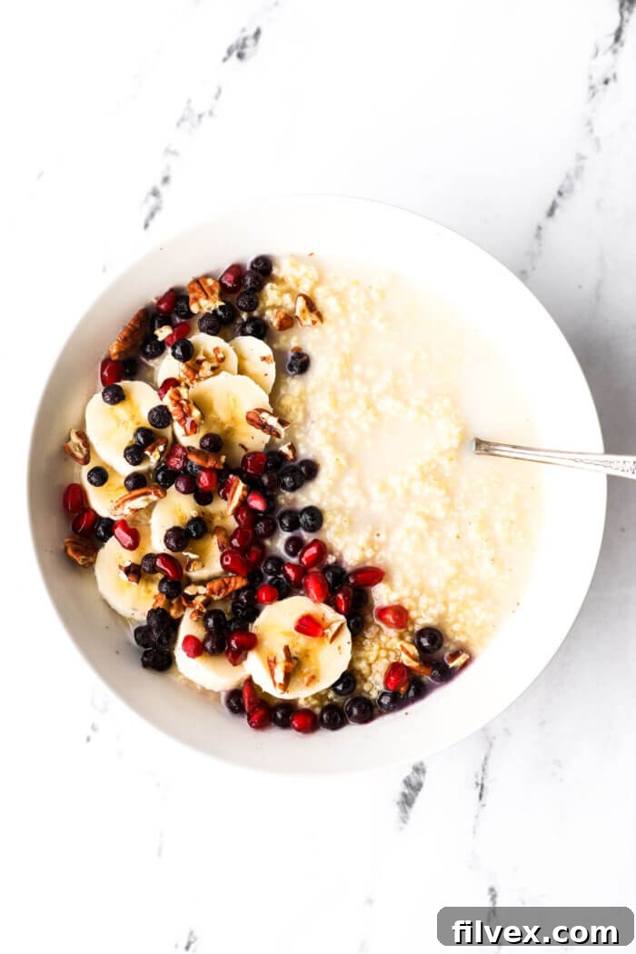 Bowl of creamy millet porridge with coconut milk, bananas, berries, pomegranate seeds and chopped pecans.