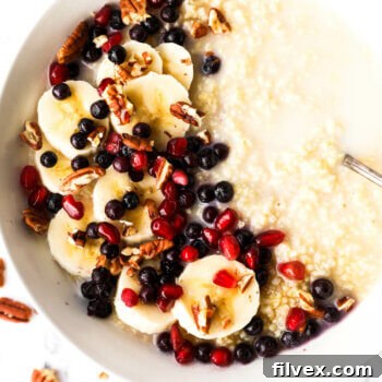 Close up image of a bowl of creamy millet porridge with coconut milk, bananas, berries, pomegranate seeds and chopped pecans, showcasing a delicious breakfast.