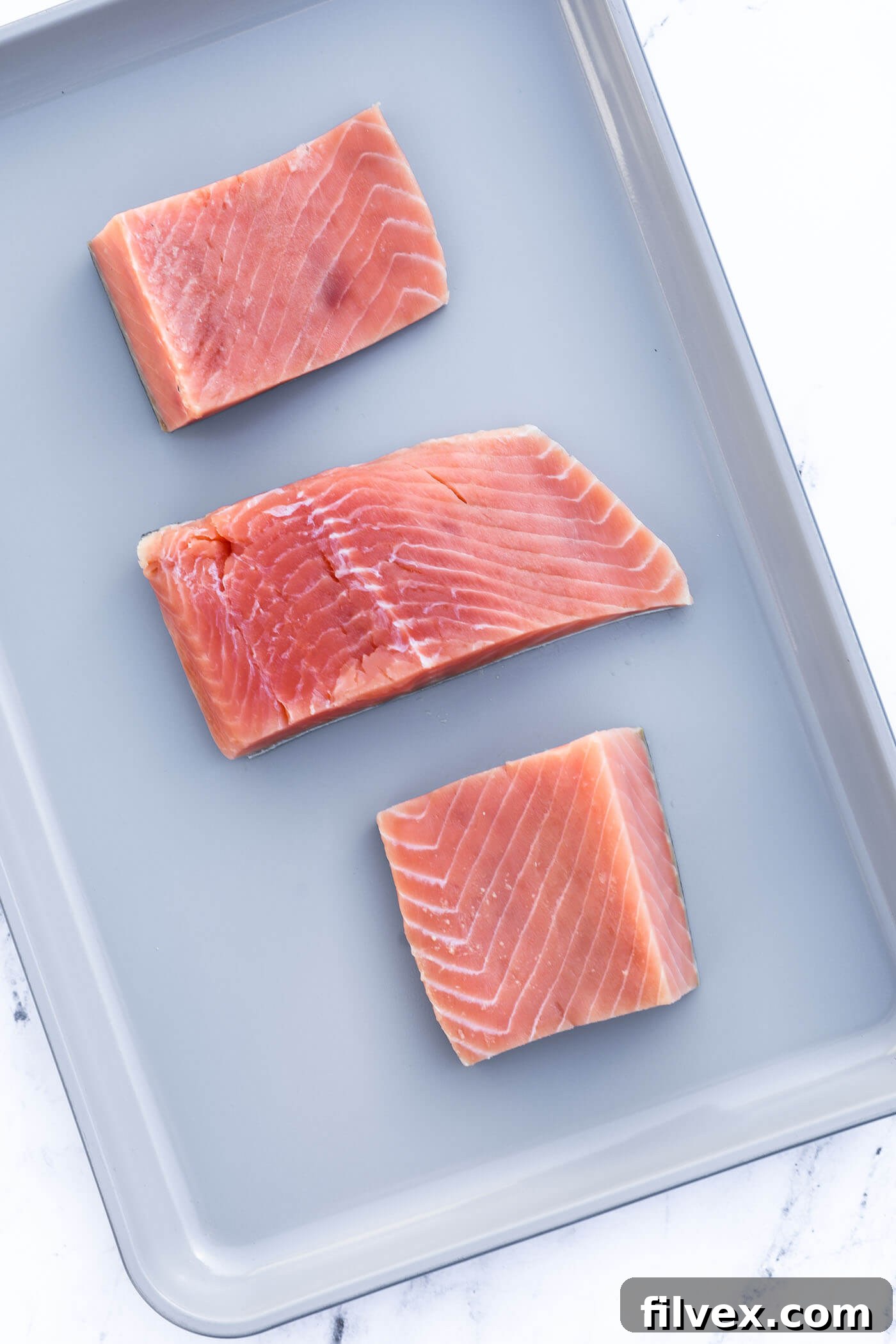 Salmon fillet being cut into individual serving portions on a cutting board.