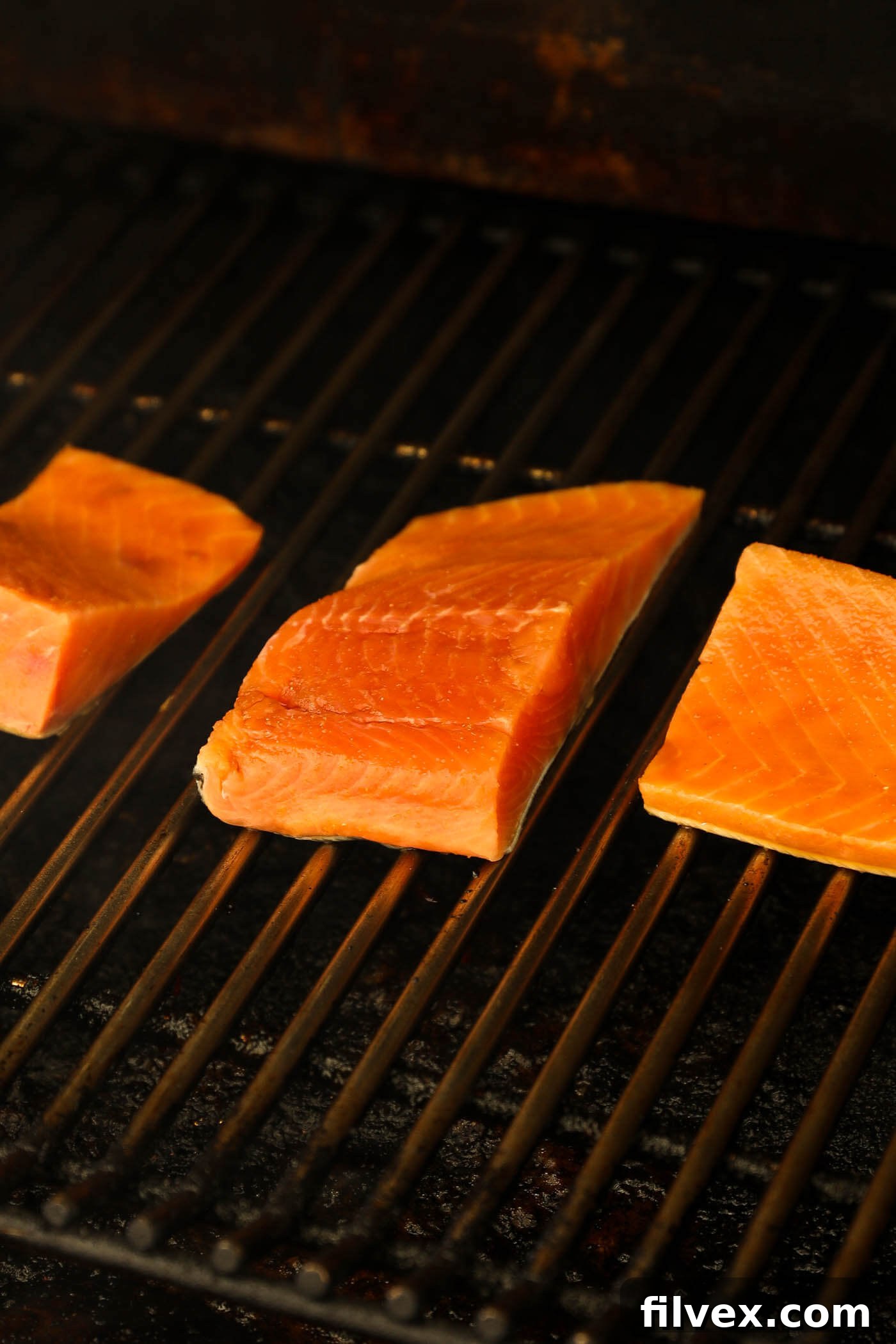 Multiple glazed salmon portions smoking on a pellet grill grate at 225°F.