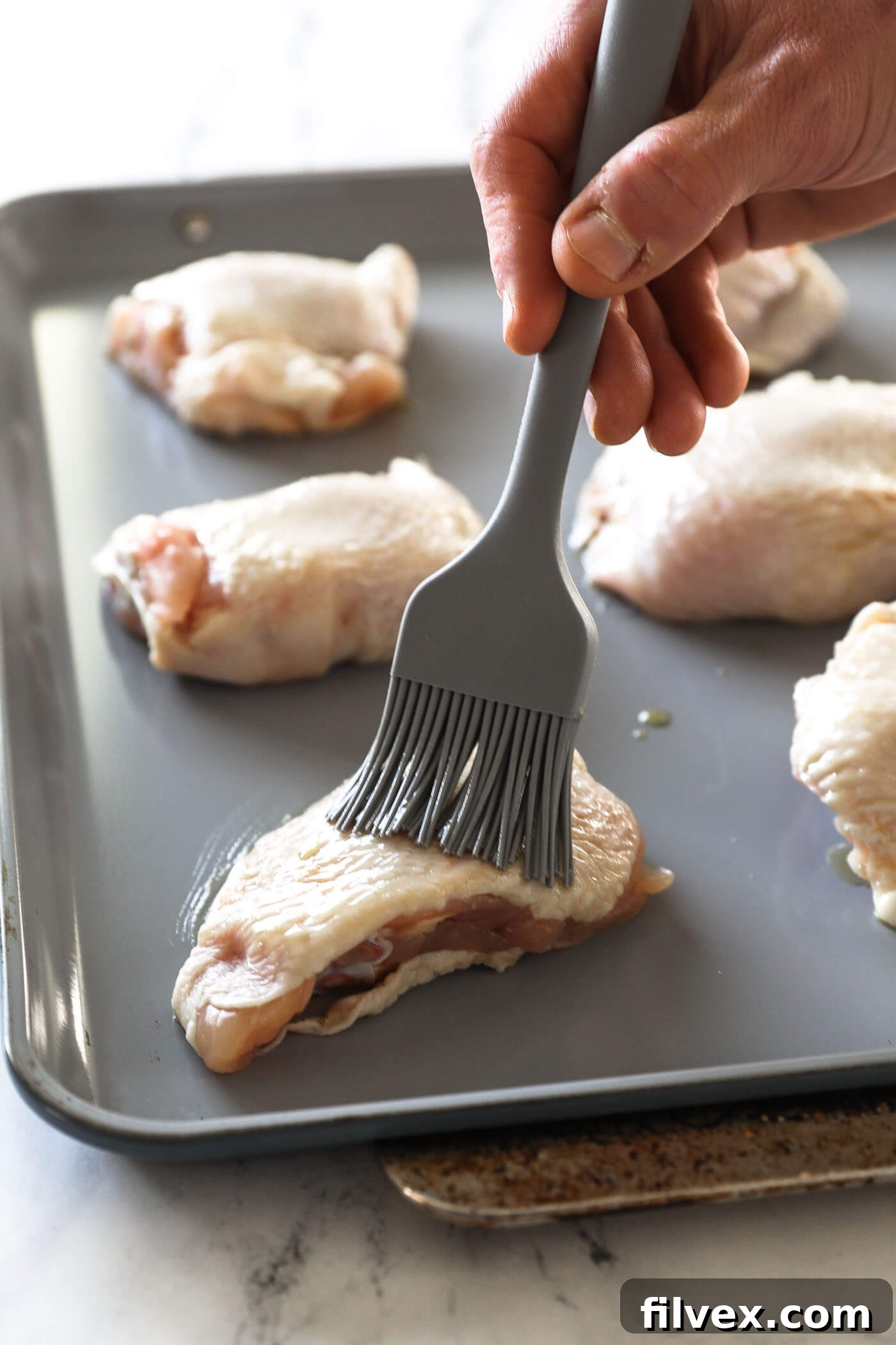 Drizzling avocado oil on chicken thighs and brushing to coat