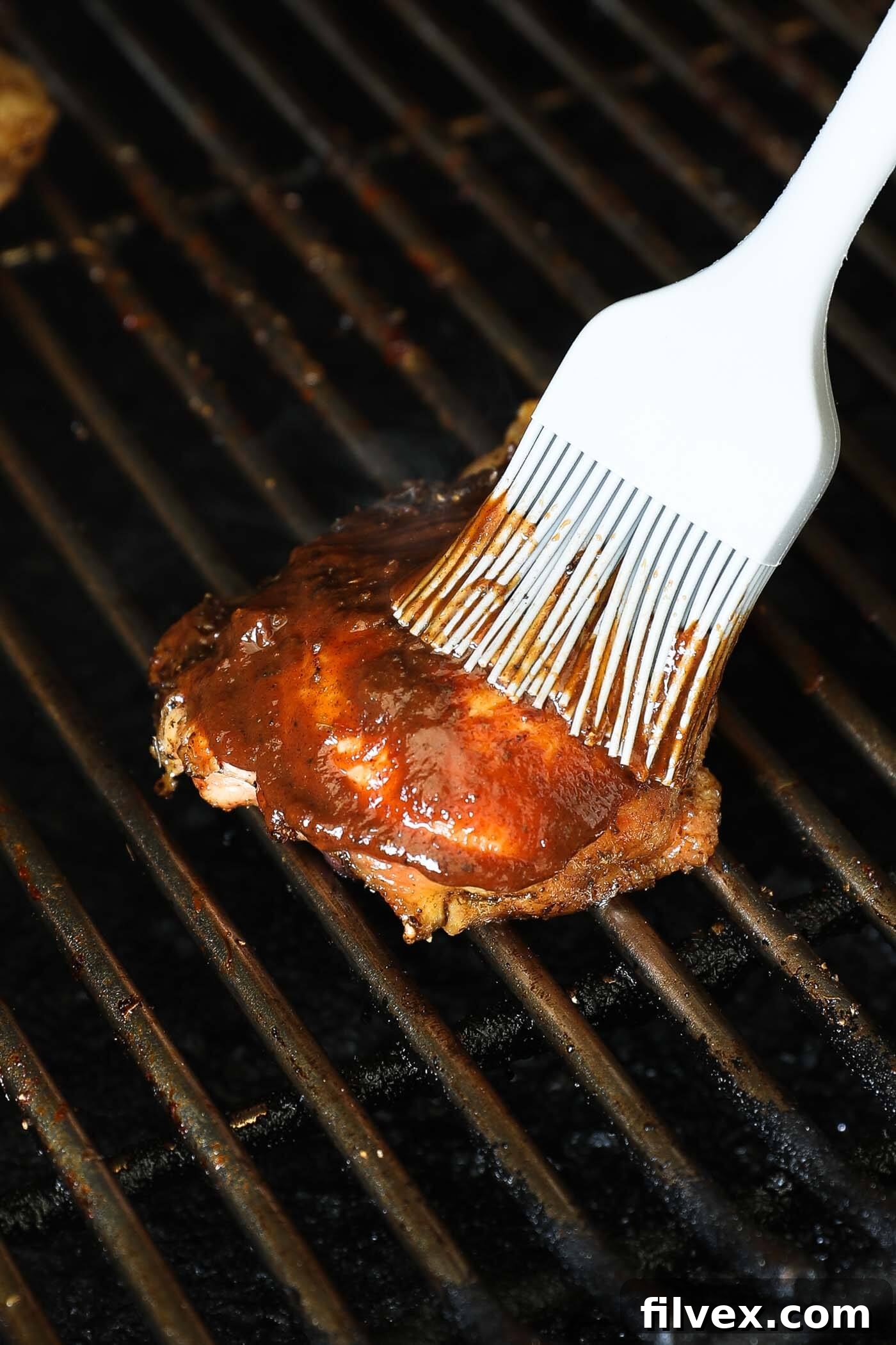 Brushing BBQ sauce on smoked chicken thighs during the final minutes of cooking