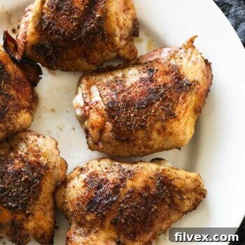 Overhead view of crispy skin smoked chicken thighs on a white plate, ready to serve