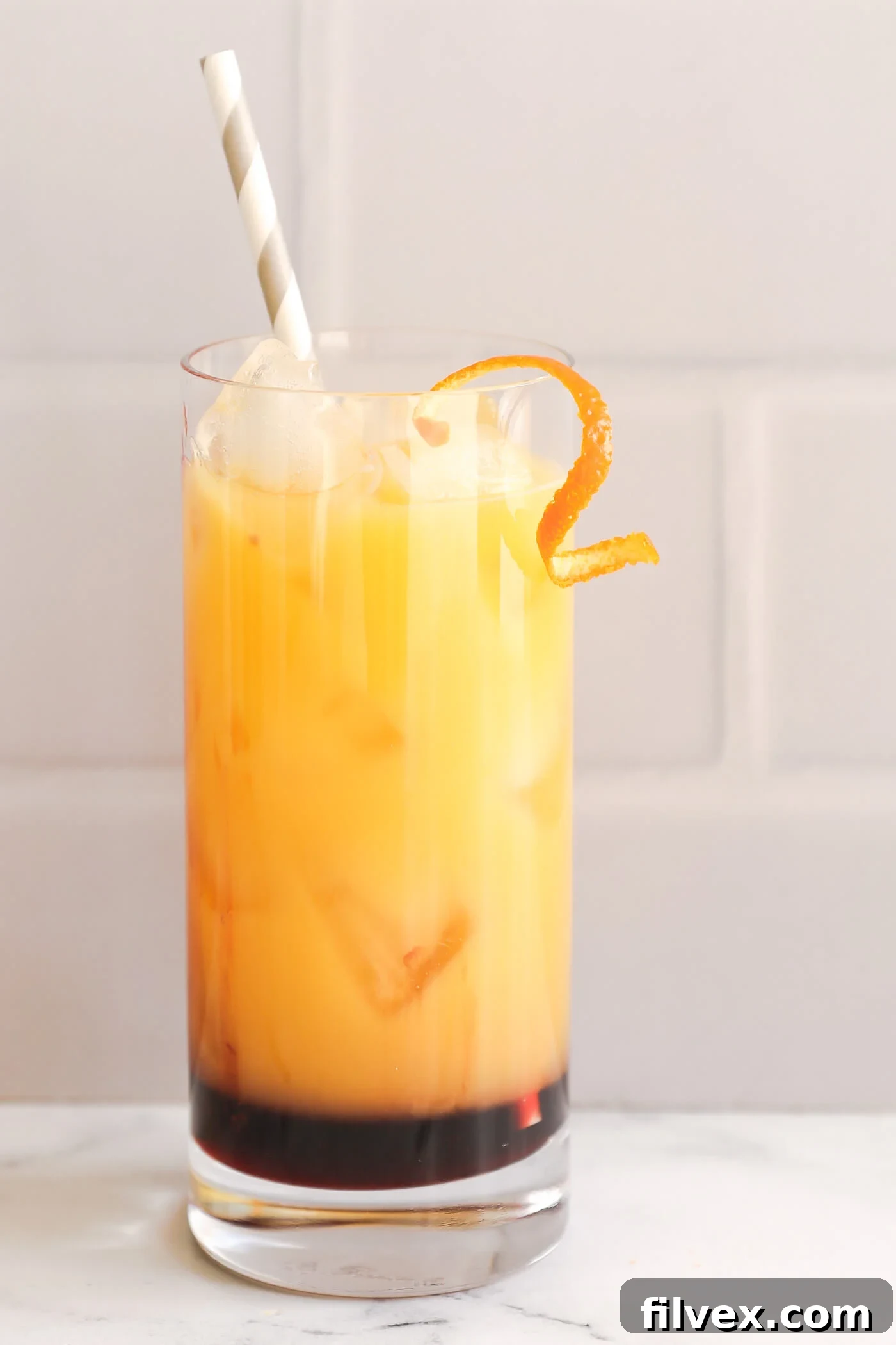 A vibrant red and orange layered Sunrise Mocktail in a clear glass, garnished with a fresh orange slice, radiating coolness and refreshment.