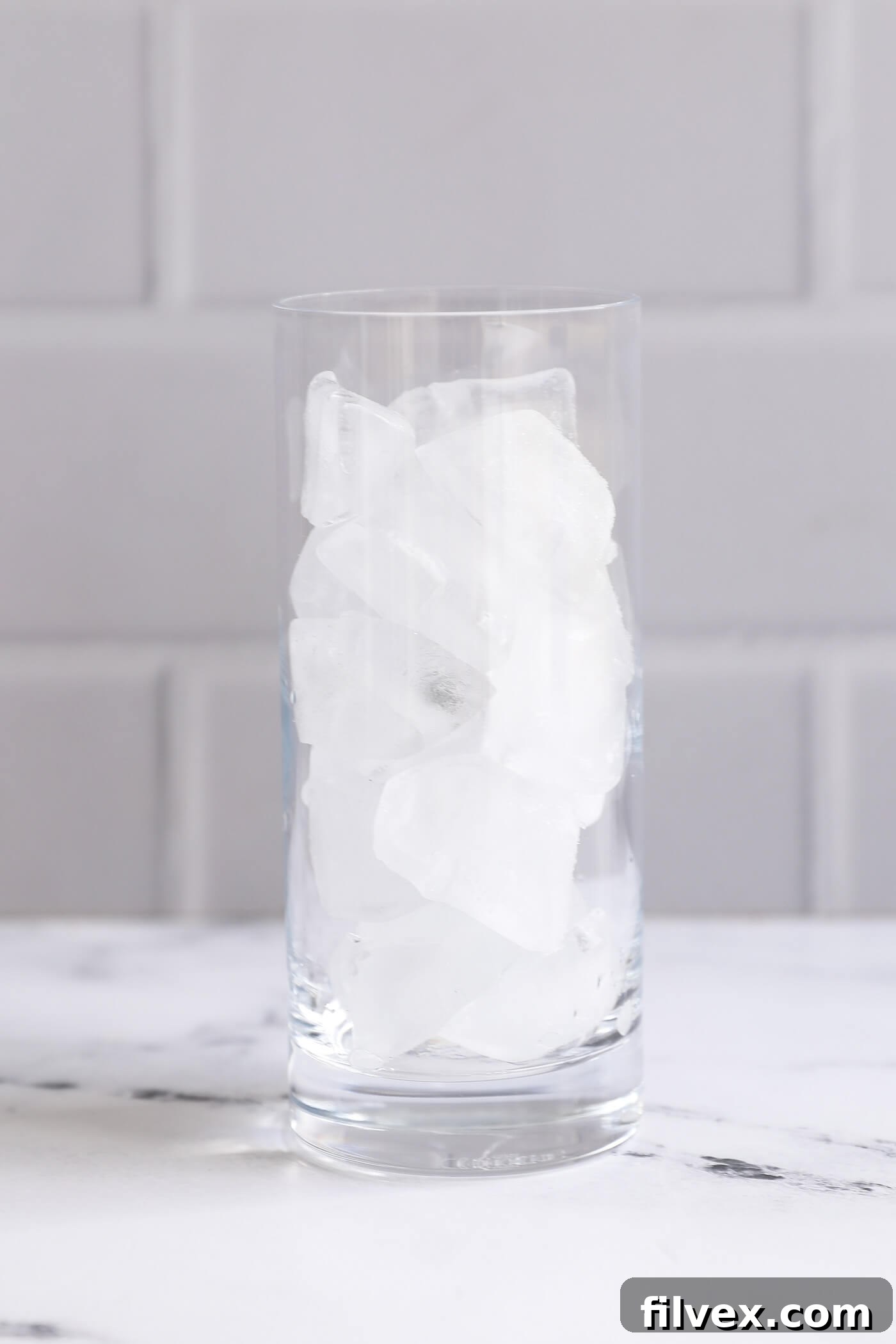 A clear glass being filled generously with sparkling ice cubes, ready to chill the mocktail.