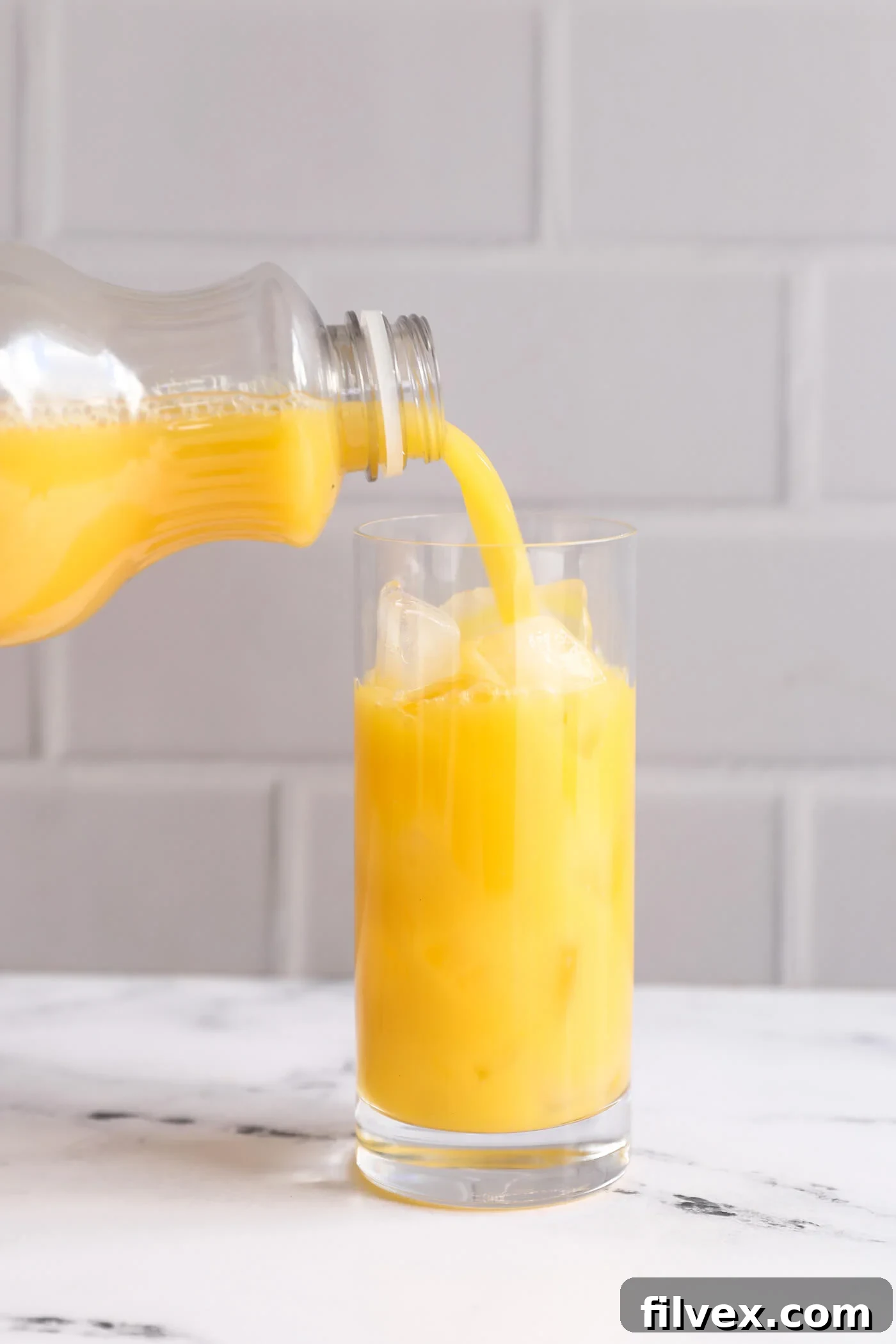 Fresh orange juice being smoothly poured into a glass already containing ice.