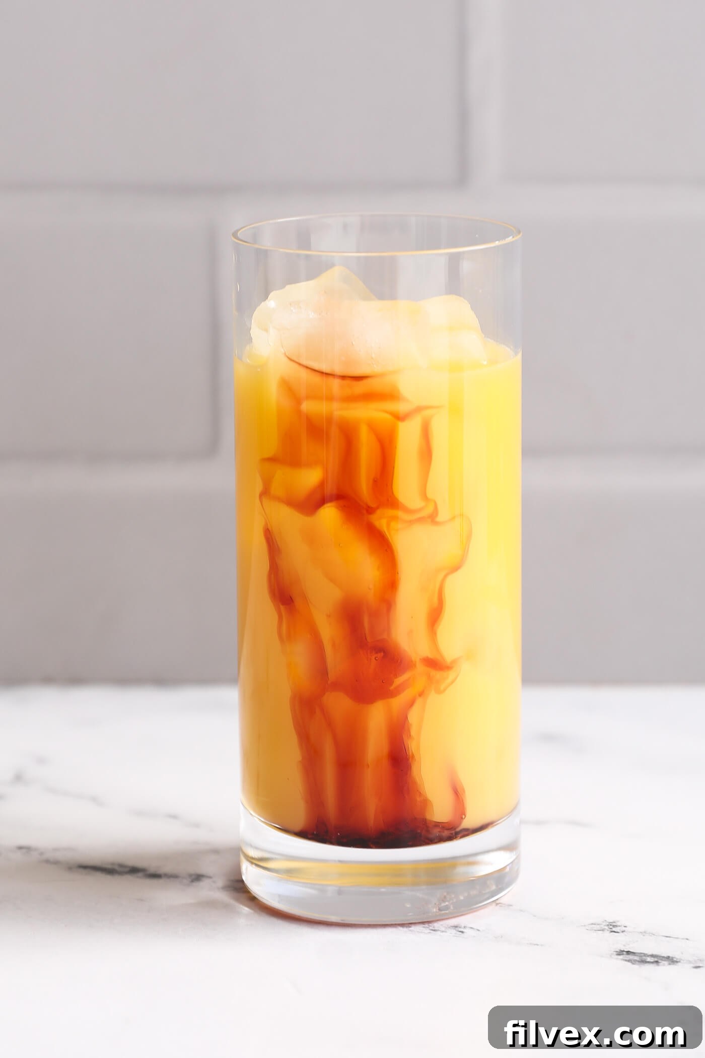 Grenadine syrup being poured directly into the center of the orange juice, creating a gradual blend of colors.