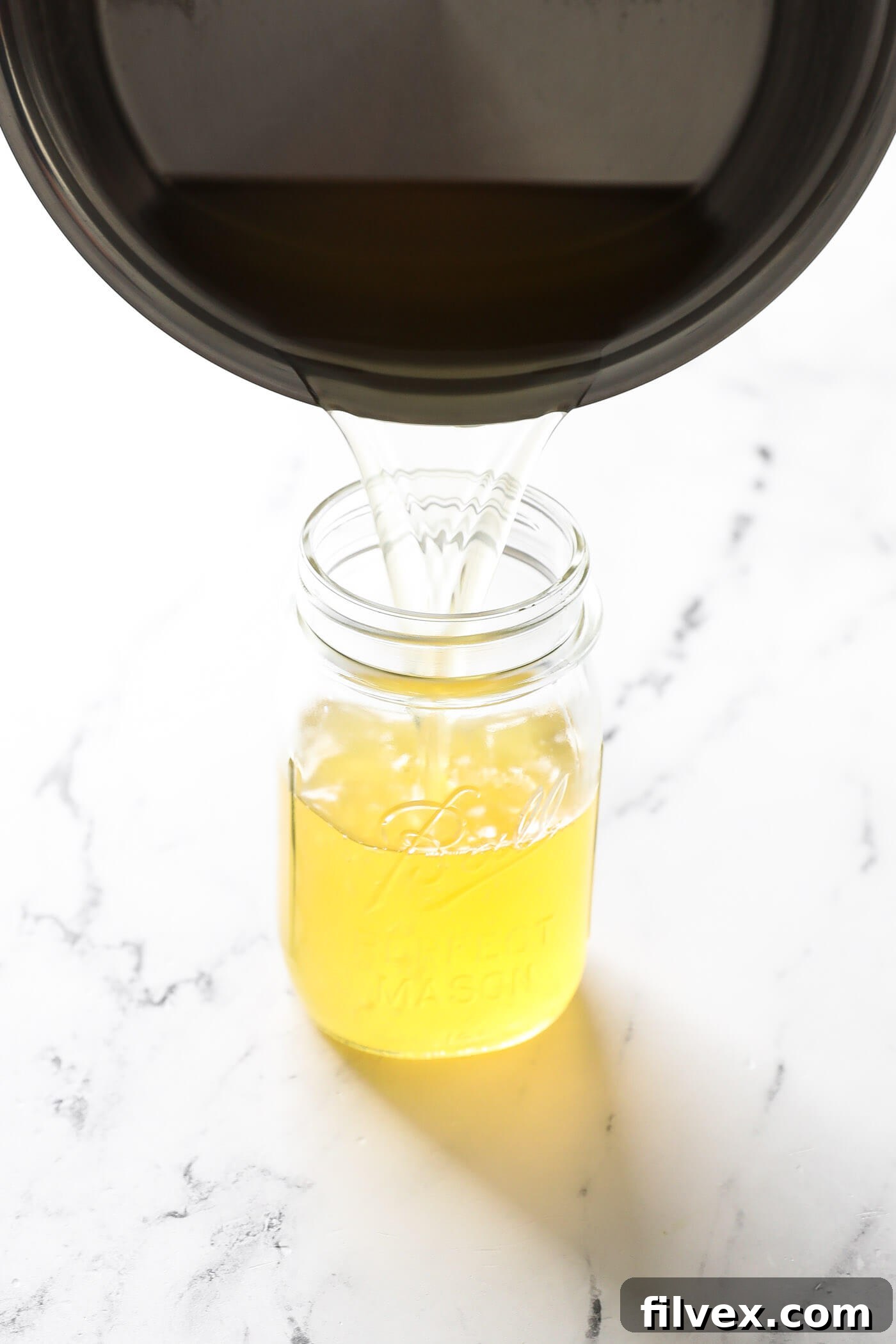 Pouring the finished honey syrup into a glass jar for storage.
