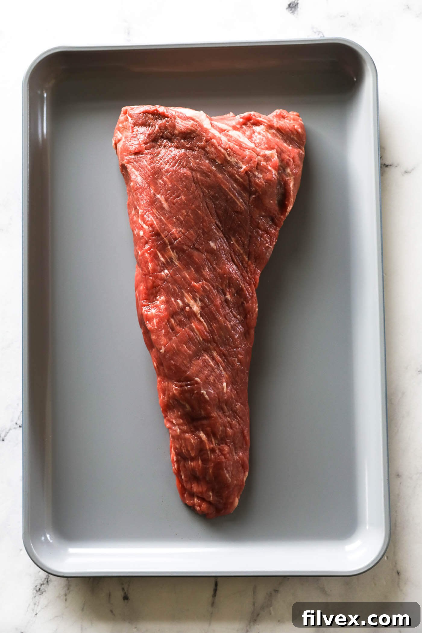 Untrimmed tri-tip roast with fatty pieces and silver skin clearly visible.