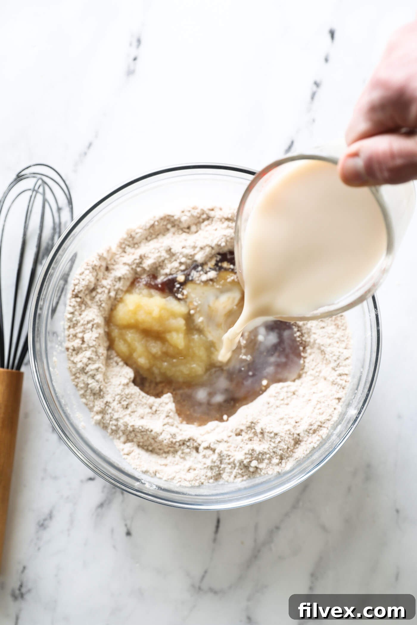 Pouring in almond milk to a mixing bowl with the ingredients to make zucchini bread.