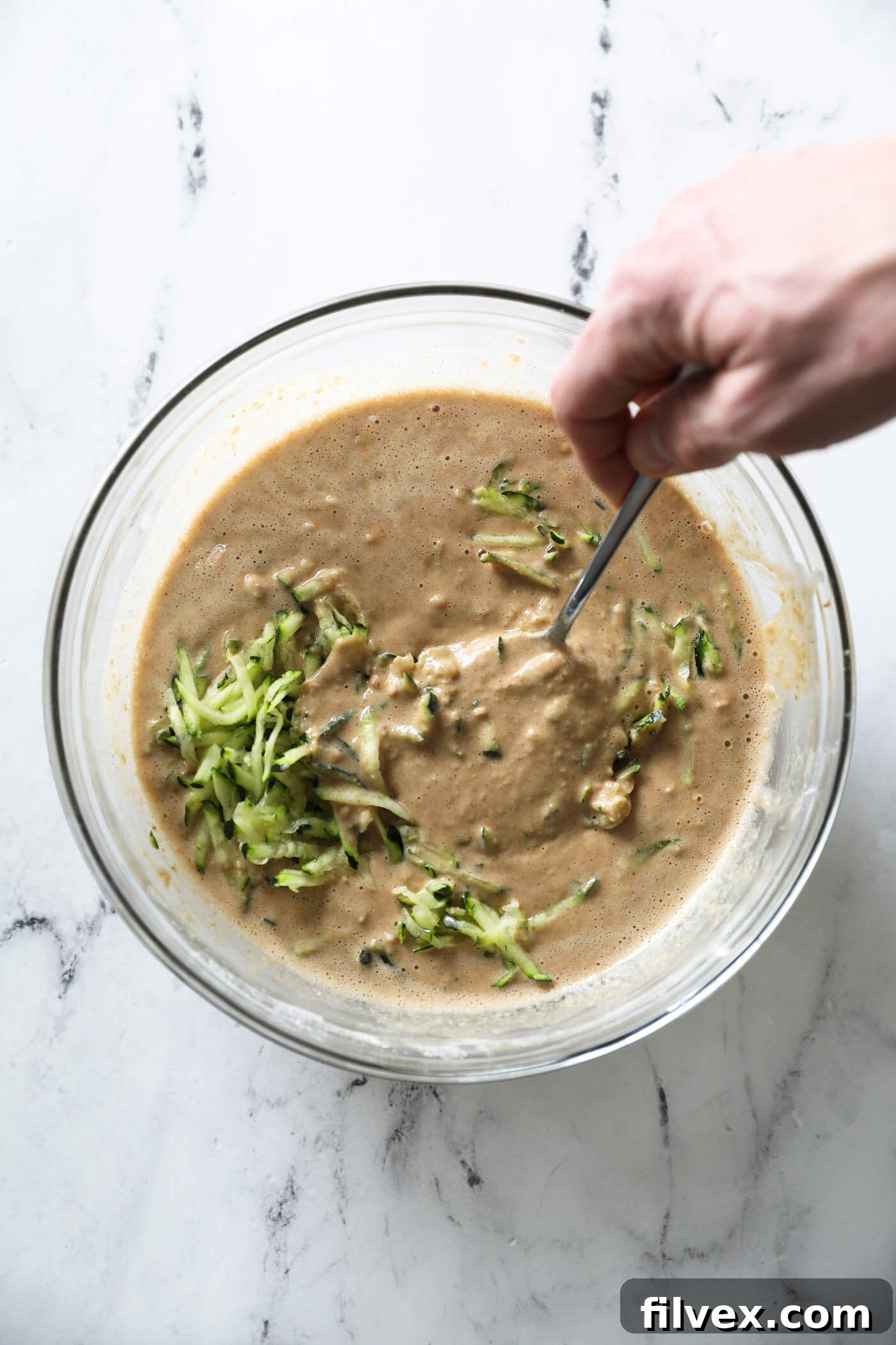 Folding the shredded zucchini into the batter.