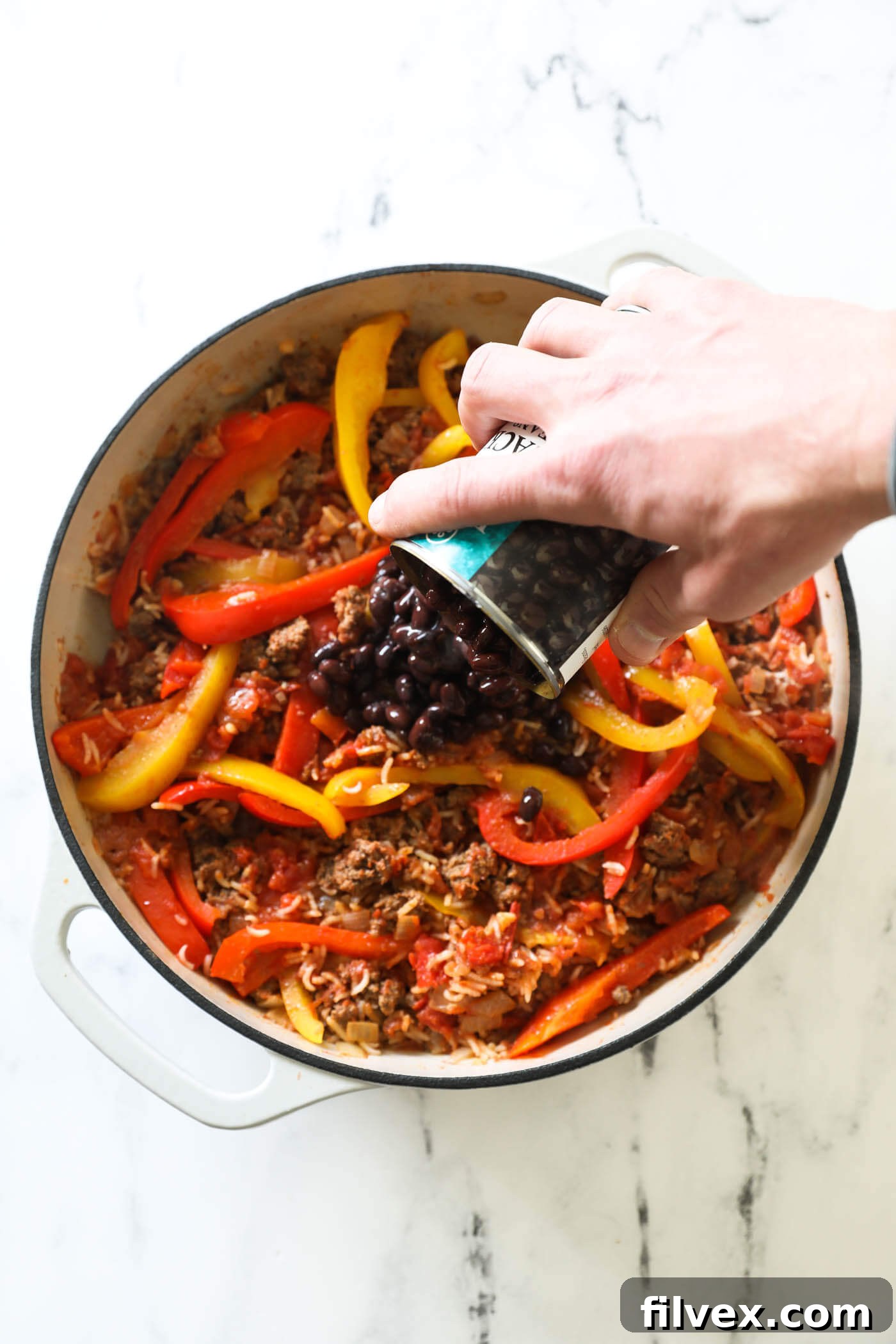 The finished deconstructed stuffed peppers dish in a pan, with black beans visibly stirred in, and optionally melted shredded cheese glistening on top, garnished and ready for serving.