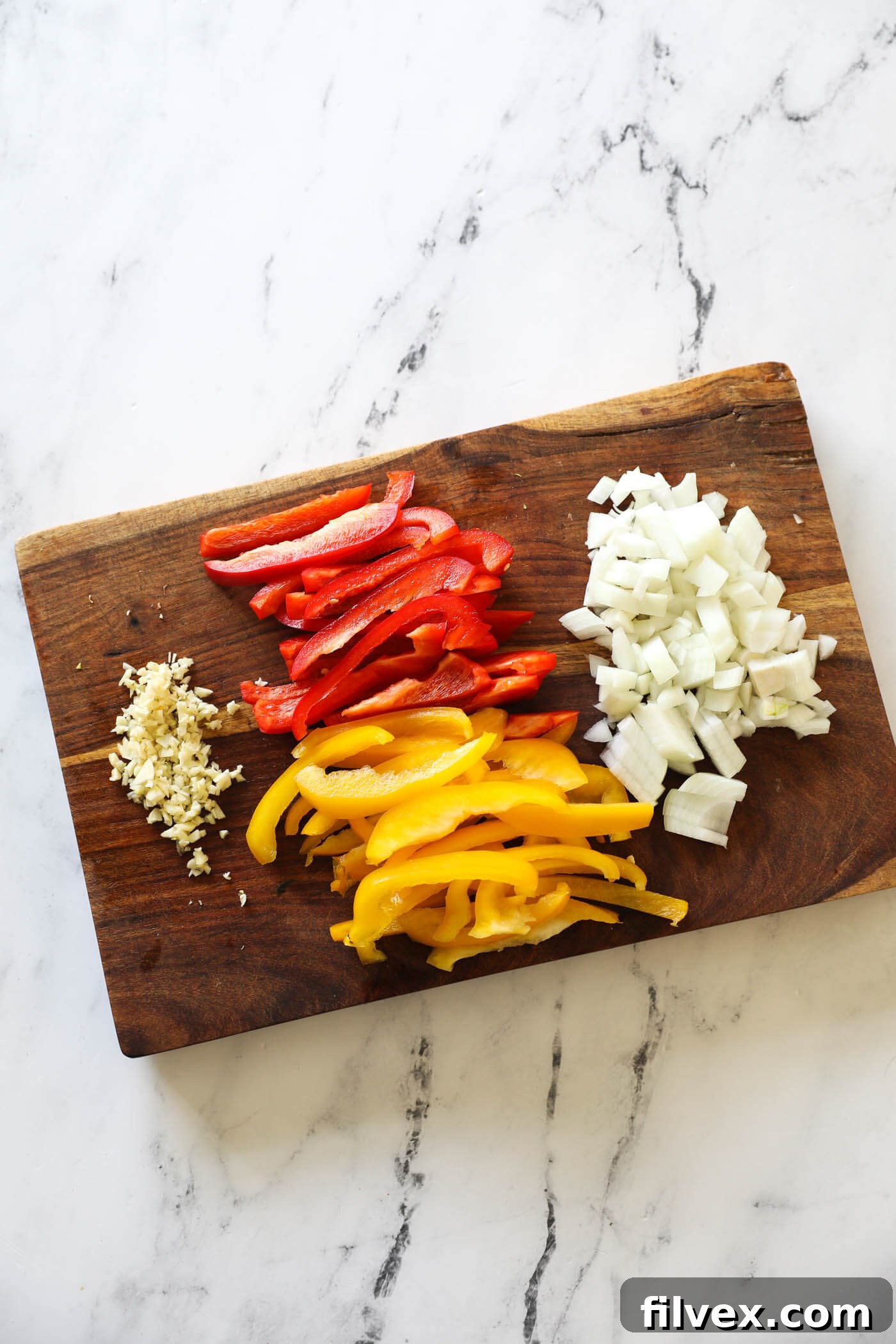 Freshly chopped garlic cloves, vibrant bell peppers cut into strips, and finely diced onion, all prepped and ready on a cutting board, illustrating the initial preparation step.